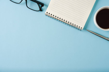 Top view of notebook, glasses, coffee and ballpoint pen on blue backgroundの写真素材