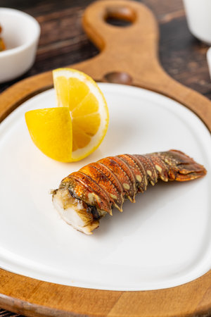 Grilled lobster tail served on white porcelain plate on wooden table with lemonの写真素材