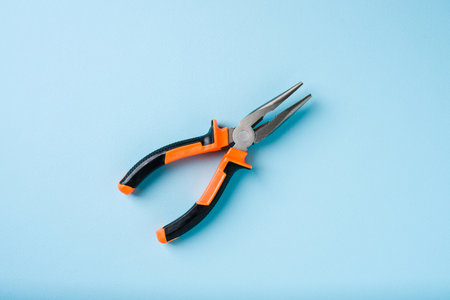 Orange and black handled needle nose pliers on a blue backgroundの写真素材