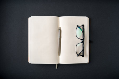 Top view of notebook, glasses and ballpoint pen on dark gray backgroundの写真素材