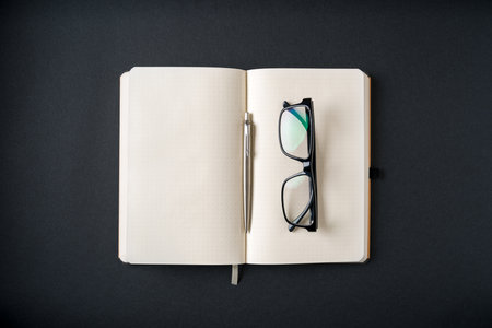 Top view of notebook, glasses and ballpoint pen on dark gray backgroundの写真素材