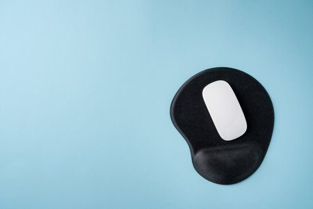 Top view of modern white mouse on black mousepad on blue table