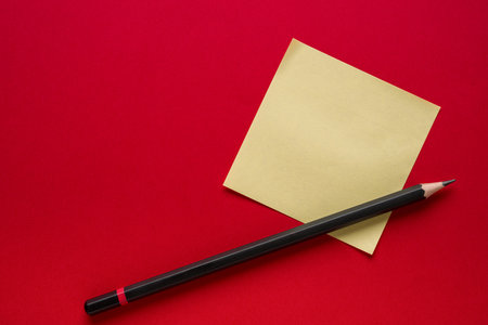 Yellow blank sticky note paper or post-it and pencil on red backgroundの写真素材