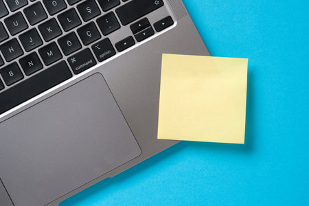 Note paper stuck to the corner of the laptop on the blue deskの写真素材