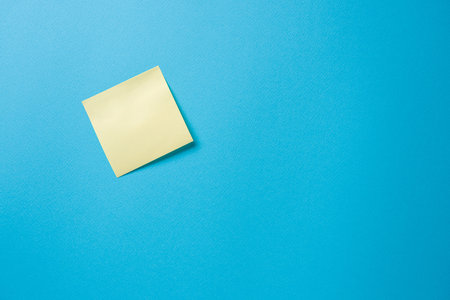 blank yellow sticky note on a blue backgroundの写真素材