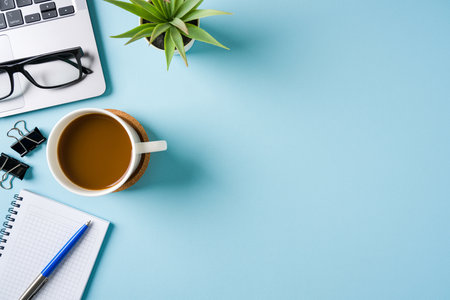 Coffee cup, laptop keyboard and various stationery items on blue office desk. Business office conceptの写真素材