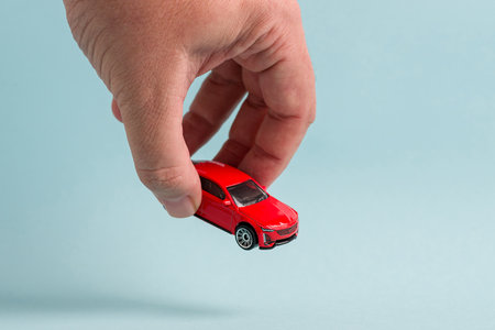 Hand holding a red toy car against a light blue background