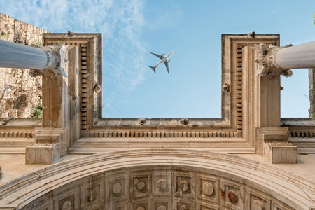 Passenger plane flying over Hadrians Gate in historic Antalya old townの写真素材