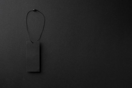 Blank black cardboard clothing tag with string on black background