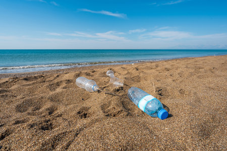 Discarded plastic bottles and cup littering the beach near the shorelineの写真素材