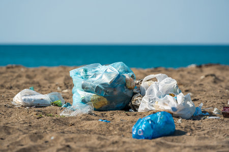 Plastic bags and bottles littered on a sandy beach by the seaの写真素材