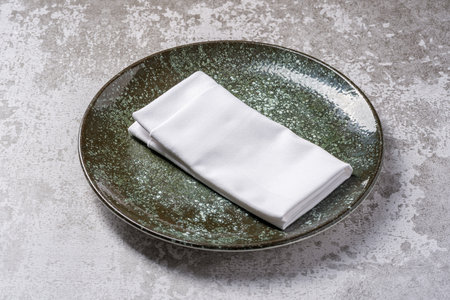 Elegant green ceramic plate with folded white napkin on stone