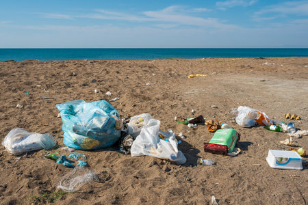 Plastic bags and bottles littered on a sandy beach by the seaの写真素材