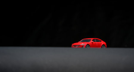 Minimal view of red toy sedan on dark background with soft lighting