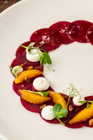 Beet carpaccio with orange slices, fresh greens and cream dotsの写真素材