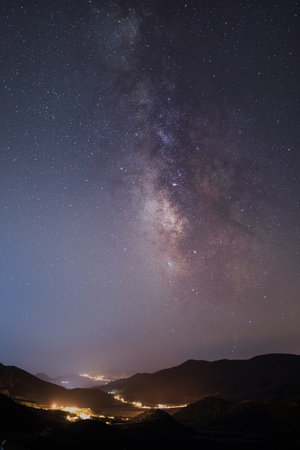 Milky Way galaxy above mountains and glowing village lights at night
