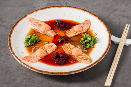 Smoked salmon sashimi plated with beetroot, scallions, and spicy sauceの写真素材