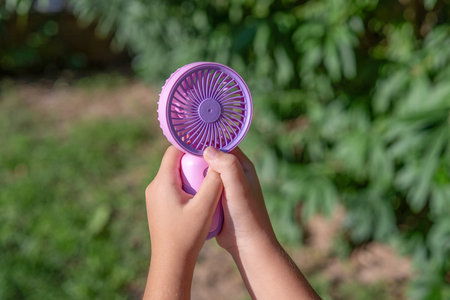Hand holding portable mini fan outdoors in sunlightの写真素材