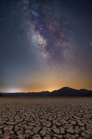 Milky Way over cracked dry lake bed with mountain silhouetteの写真素材