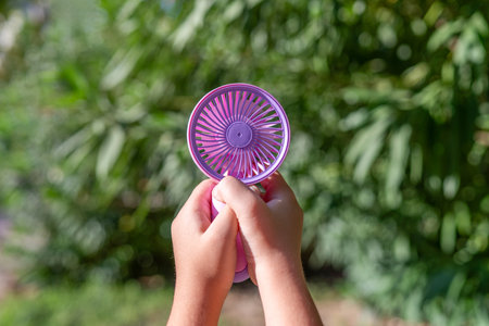 Hand holding portable mini fan outdoors in sunlightの写真素材
