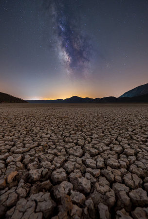 Milky Way over cracked dry lake bed with mountain silhouetteの写真素材
