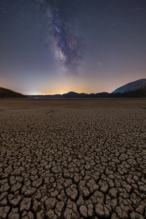 Milky Way over cracked dry lake bed with mountain silhouetteの写真素材
