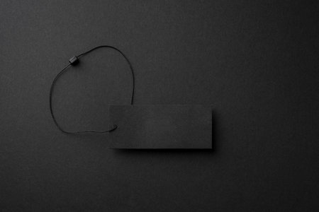 Minimalist black cardboard clothing tag with string on dark backgroundの写真素材