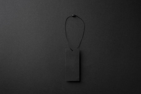 Minimalist black cardboard clothing tag with string on dark background