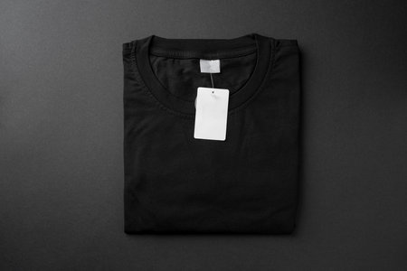 Folded black t-shirt with blank paper tag on dark backgroundの写真素材