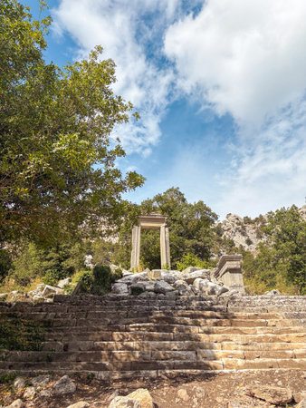 The ruins of Hadrian Gate in the ancient city of Termessos, framed by trees and a rocky foregroundの写真素材
