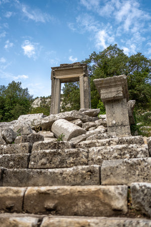 The ruins of Hadrian Gate in the ancient city of Termessos, framed by trees and a rocky foregroundの写真素材