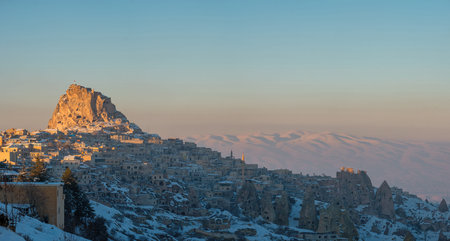 Snow covered Uchisar Castle overlooking Cappadocia village at sunsetの写真素材
