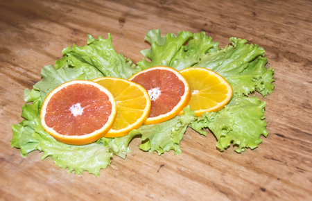 cut slices of red and orange on green leaves of lettuce on a wooden backgroundの写真素材