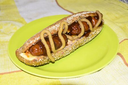 hot dog in a bun with ketchup and mustard lies on a green plate on a yellow tableclothの写真素材