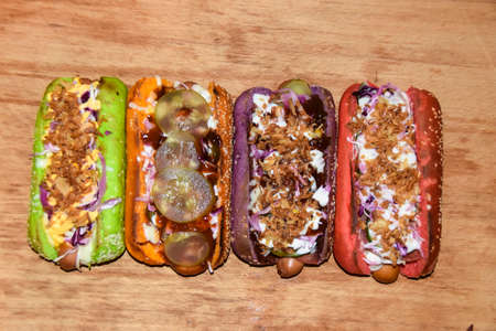 hot dogs assorted multi-colored buns different toppings on a wooden background