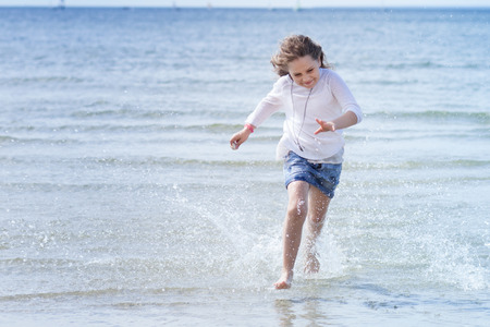Cute girl run with splashes at the coastの写真素材