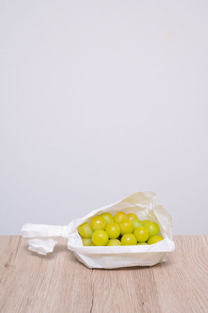 Green grapes in a package on a wooden table and white wall backgroundの写真素材