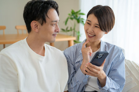 Happy asian young couple using smartphone in living room at home.の写真素材