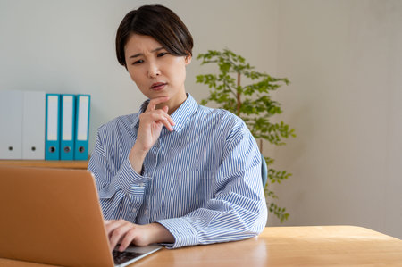 Portrait of businesswoman looking at laptop while sitting at desk in officeの写真素材