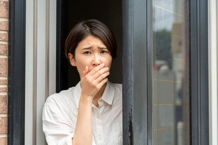 Woman looking through the window in the city and sneezing.の写真素材