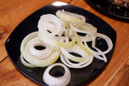 Sliced onions on a black plate on a wooden table.の写真素材