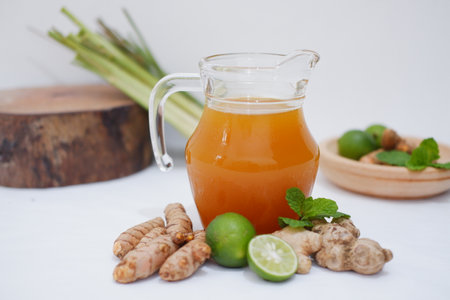 Ginger juice in a glass jug with fresh ginger and lime on white background