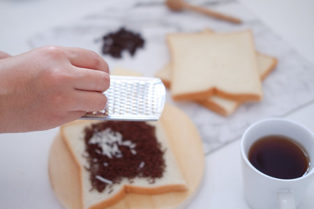 Hand grating chocolate cake with grater and cup of coffee.の写真素材