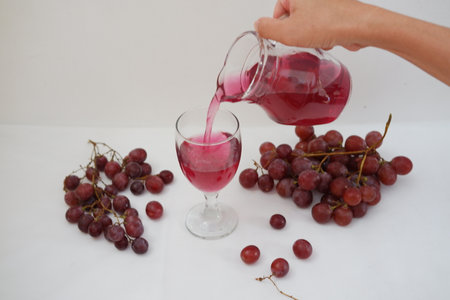 Pouring red wine into glass with bunch of grapes on white backgroundの写真素材