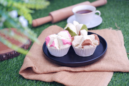 Cup of tea with marshmallows on black plate on green grassの写真素材