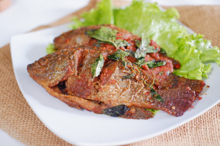 Fried fish with tomato sauce and herbs on the white plate.