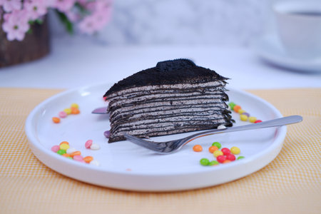 Chocolate crepe cake on white plate with spoon and colorful candiesの写真素材
