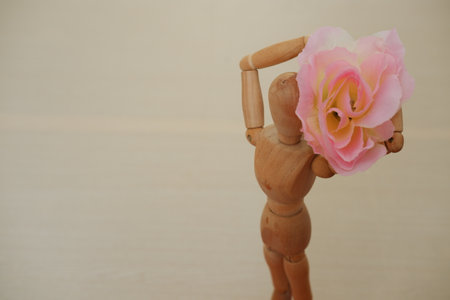 Wooden mannequin holding a pink rose on a wooden backgroundの写真素材