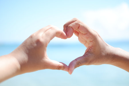 Hands forming a heart shape with the sea in the background.