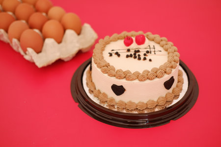 Cake with cherry on top and eggs on a red background.